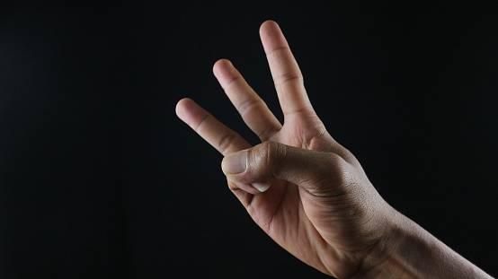 Male hand gesture number three closeup isolated on a black background