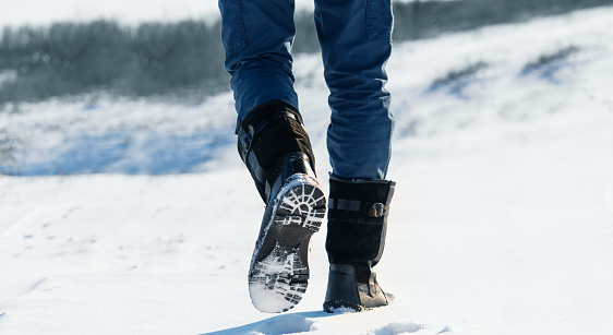 Close up of men's winter boots in snow. The man in boots walks along a snowy winter road. Sunset in the winter forest.