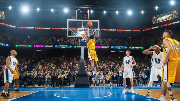 jugador superestrella de baloncesto nacional afroamericano anotando un poderoso gol de volcada con ambas manos frente a una audiencia de fanáticos que lo vitorean. cinemática deportiva filmada con acción de visión trasera. - sport watching television broadcasting television fotografías e imágenes de stock