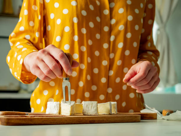 Female in yellow polka dot shirt with a cheese on table in kitchen stock photo