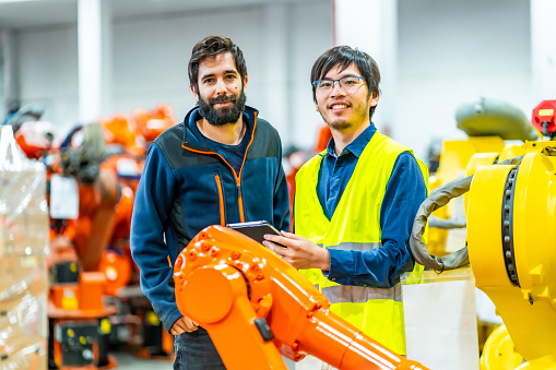 Portrait of two young multi-ethnic engineers in a industrial robot industry looking at camera and smiling