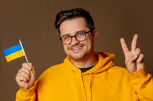 Stylish man in yellow hoodie with Ukrainian flag on brown background