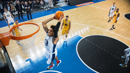 Close up image of professional basketball player about to do slam dunk during basketball game in floodlight basketball court