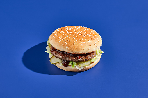 Beef burger blue background with hard shadow. American junk food minimal style. Hamburger trendy style.  Simple burger colour background