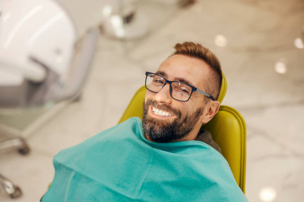 porträt eines patienten, der in der zahnarztpraxis auf einem stuhl mit perfektem lächeln sitzt. - dentists chair dentist office chair orthodontist stock-fotos und bilder