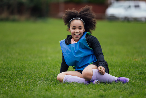 A medium, portrait shot of a young boy while playing football for a children's team in the North East of England. He is standing, looking and smiling at the camera on the sports field wearing a sports bib.
