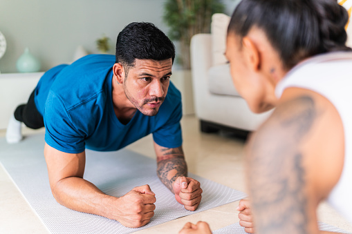 Young man doing exercise with his wife in living room at home