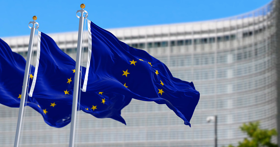 European union flag waving with European Commission headquarters blurred in the background. Political and economic union. 3d illustration render. Rippling fabric. Selective focus