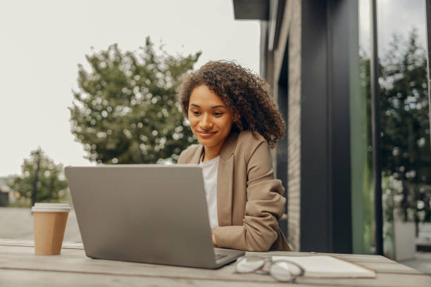 Smiling female freelancer working on laptop while sitting in cafe terrace. Distance work concept