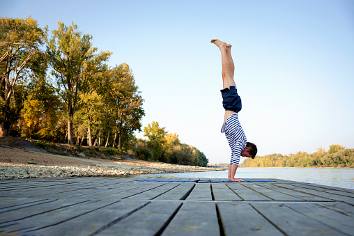 Mid aged man practicing yoga outdoor. Caucasian man using yoga mat and doing yoga at nature. Yoga handstand.