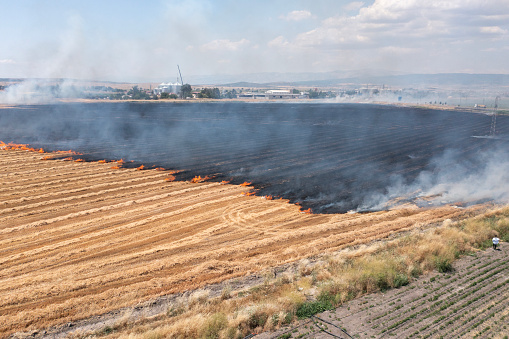 A farmer in his tractor cultivates the earth trying to contain a wheat field fire believed to be ignited by the harvester striking a rock.