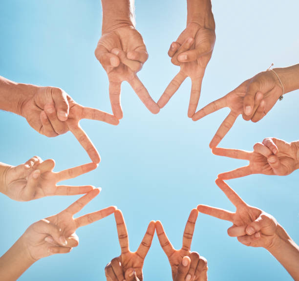 istock Teamwork, community and group support with fingers in a star shape from below against a blue sky background. A diverse crowd of people with hands joined together for motivation, unity and peace 1795138596