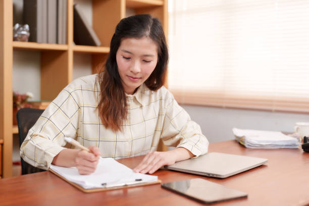 istock Asian female office worker, sitting signing documents related company work, was assigned project, has computer laptop is on desk because it's during working hours so we're ready work all time. 1795160608