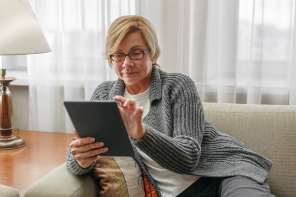 istock Mature woman smiling and using tablet in living room while sitting on sofa 1795172488
