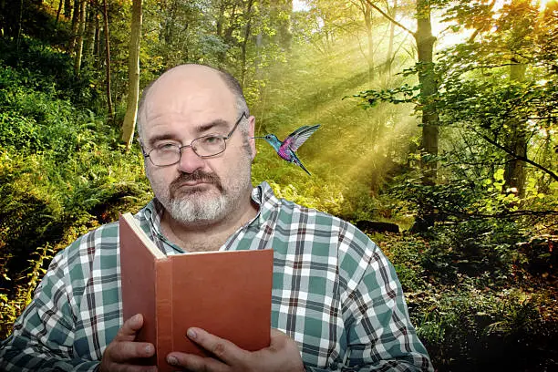 Photo of Mature man reads in the woods with hummingbird