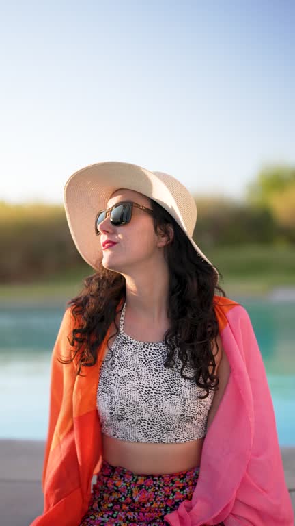 beautiful mid adult hispanic woman sitting relaxed at the  poolside at sunset