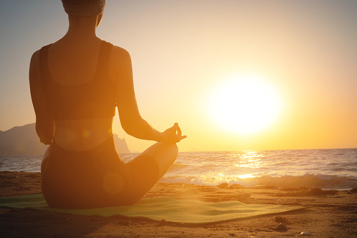 meditation and yoga on the beach. concept of doing yoga on summer vacation or vacation by the sea. woman in lotus position at dawn.
