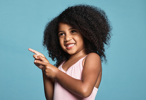 Advertising, hand and child with smile, happy and finger for blue mockup studio background. Face of a young African girl in happiness while pointing to show attention to marketing and mock up space