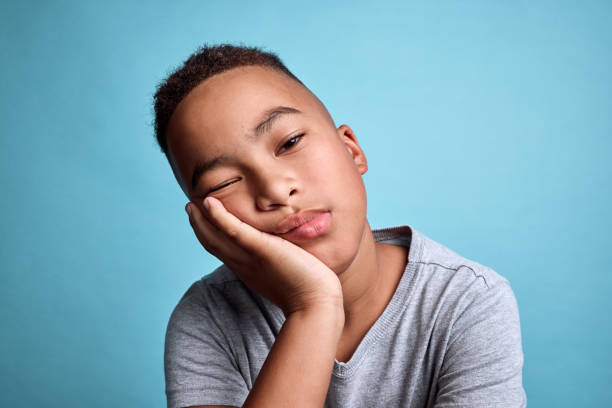 istock Tired child face on blue background, depression while lazy thinking and rest on hand in studio. Sad black boy with adhd, bored kid with depressed insomnia and mental health fatigue in young children 1795209497