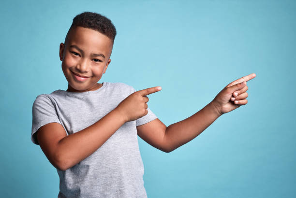 istock Mockup space, idea and happy boy pointing in a studio with a solution, advertising and marketing. Portrait of happiness, smile and young african kid with a positive thought and with blue background. 1795209502