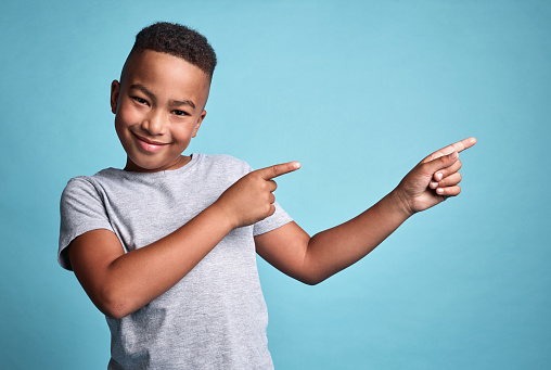 Mockup space, idea and happy boy pointing in a studio with a solution, advertising and marketing. Portrait of happiness, smile and young african kid with a positive thought and with blue background.