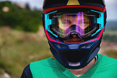 Close-up portrait of a MTB and downhill racer on a mountain trail. Colored full helmet, clear glasses and smiling guy
