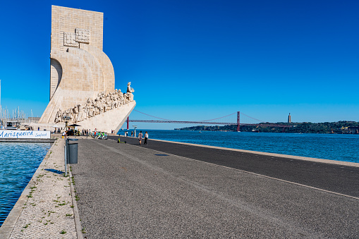 Lisbon, Portugal - Sep 29, 2023: View of Padrão dos Descobrimentos and 25 de abril bridge in summer day in the sunshine with tourists.