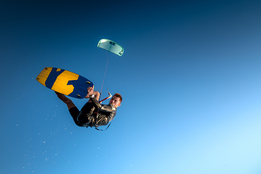 Sports kitesurfer in the air doing a trick with a wakeboard, rider in a wetsuit on a clear blue sky in a parachute jump, looking at the camera. Water sports.