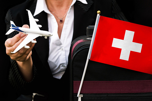 business woman holds toy plane travel bag and flag of Switzerland.