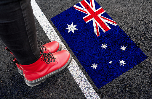 a womman with a boots standing on asphalt next to flag of Australia and border