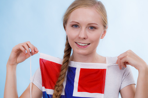 Blonde girl braid hair with norwegian flag, on blue. Scandinavian people.