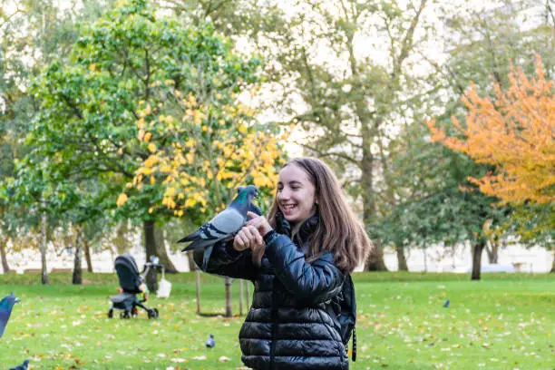 Cheerful Teenage Girl on Sunny Autumn Day Playing with Pigeons and Duck in St.James Park in London, UK