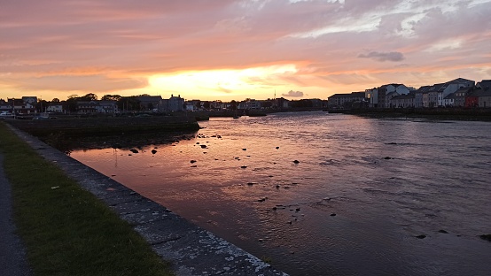 A serene riverside sunset in Galway, Ireland, with vibrant skies reflecting on calm waters.