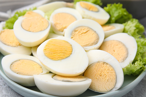 Plate with fresh hard boiled eggs and lettuce on light grey table, closeup