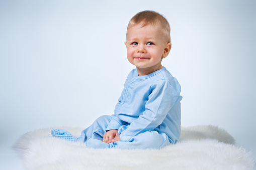 Eight month baby sitting on fur carpet on white and blue background