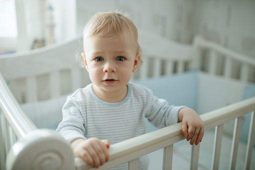 One year baby standing in bed portrait. White home interior.