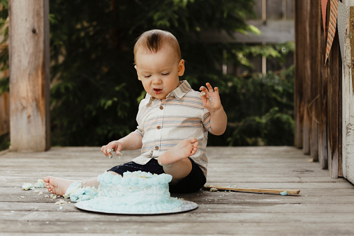 A one~year~old baby boy makes a face as he puts his foot in his birthday cake.