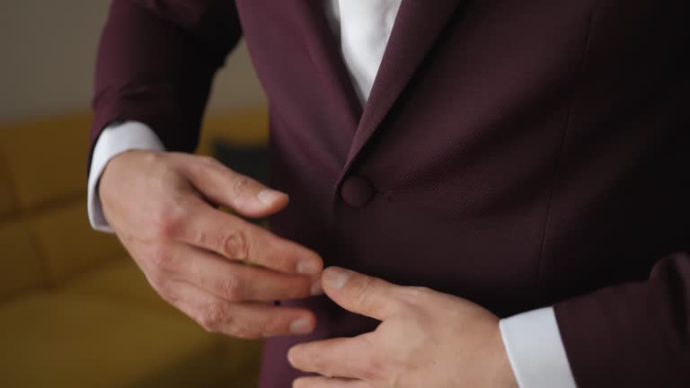 Close-up shot of the groom's hand fastening a button on a velvet jacket