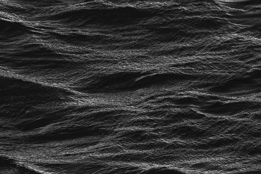 Close-up black and white photograph of a body of water with rolling waves crashing against the shore
