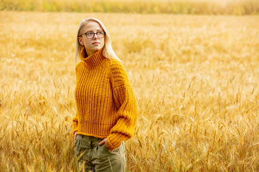 Stylish girl in eyeglasses and yellow sweater in wheat field