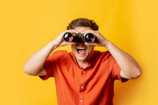 istock Guy in orange shirt watch in binoculars on yellow background 1795332780