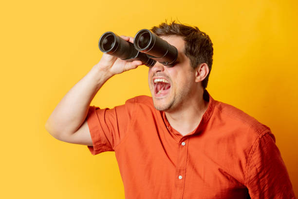 istock Guy in orange shirt watch in binoculars on yellow background 1795332969