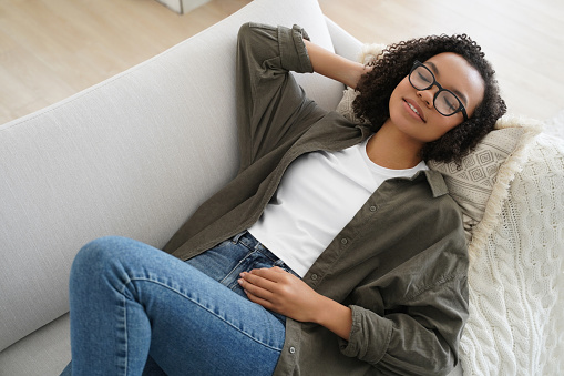 Relaxed Black woman with glasses resting on couch, eyes closed, peaceful