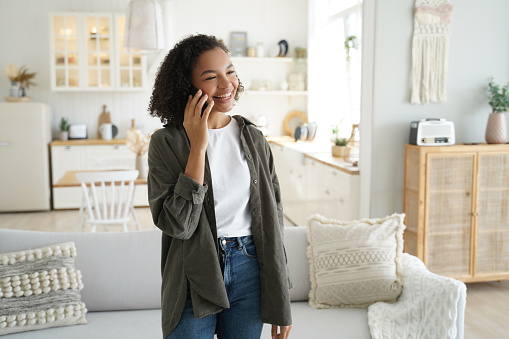 Smiling Black woman chatting on phone in a stylish, cozy living room