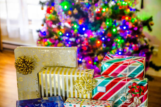 Many colorful gifts at the bottom of lit Christmas tree