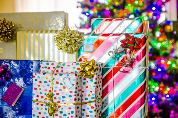 Many colorful gifts at the bottom of lit Christmas tree