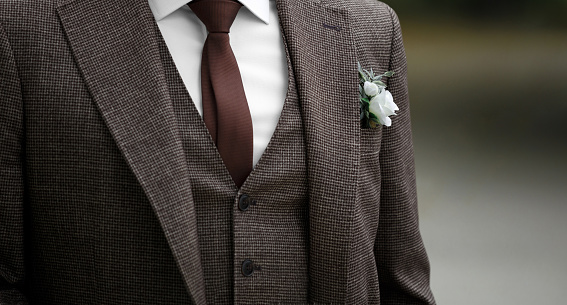 The groom is wearing a stylish wedding suit in brown tones, a tie, and a boutonniere in his buttonhole. Elegant wedding fashion.