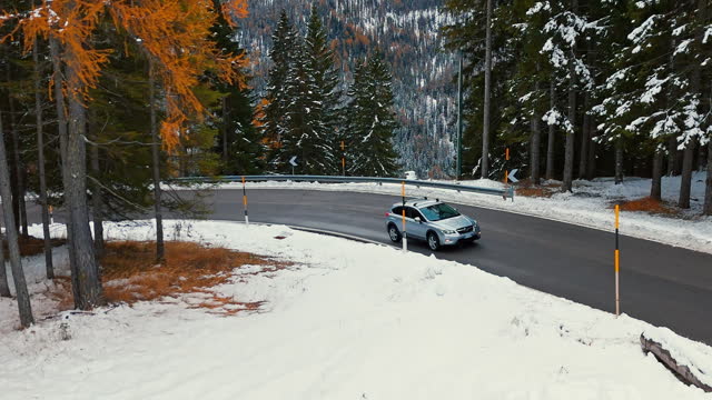 AERIAL Drone Shot of Car Driving on Asphalt Road against Larch Forest and Snowy Rocky Mountain in Dolomites