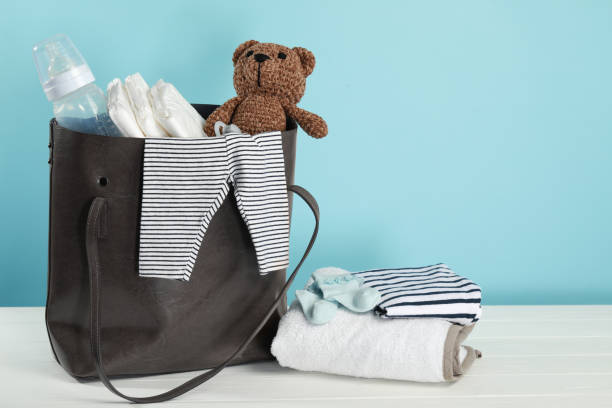 istock Mother's bag with baby's stuff on white wooden table against light blue background 1795377514