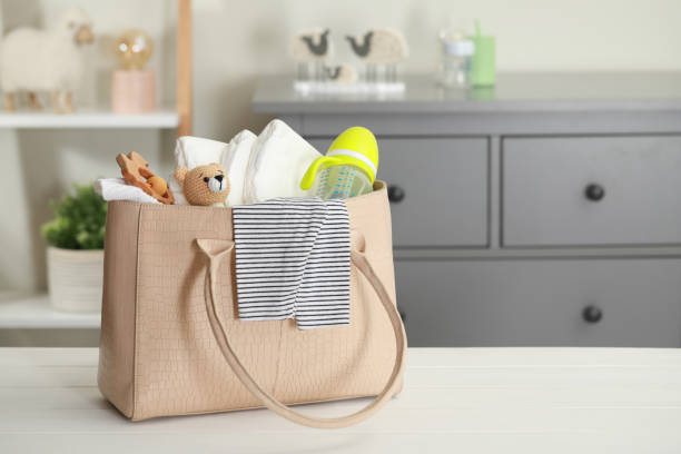 Mother's bag with baby's stuff on white wooden table indoors. Space for text